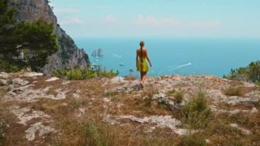 Capri Adası 'nda yürüyüş yapan ve aşağıdaki uçurumun kenarından bakan bir kız. Uçsuz bucaksız deniz manzarasının tadını çıkaran bir kadın. Sonsuz okyanus gökyüzüyle buluşuyor. İtalya..