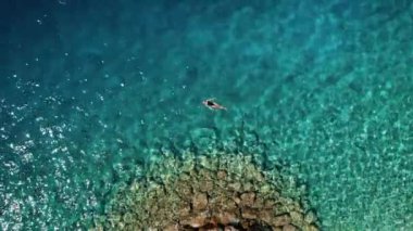 Turkuaz denizde tek başına yüzmek. Yukarıda, bir yüzücü kadın Adriyatik sularında yalnızlığın tadını çıkarıyor. Yukarıdan aşağıya hava manzaralı. Hırvatistan 'da Makarska Riviera.