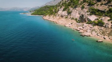 Mavi deniz suyundaki kayalık plajın yakınındaki SUP sörf tahtasında yüzen çift. Tropik adadaki aile tatilde eğleniyor ve kürek çekiyor. Makarska Riviera Hırvatistan.
