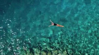 Su yüzeyinde kristal berraklığında turkuaz bir okyanusta yüzen siyah mayo giymiş genç bir kadın. Hırvatistan 'da cennette tatilde olan mutlu kız.