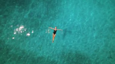 Kadın berrak sularda yüzüyor. Havadan aşağıya, turkuaz denizde mayo giyen bir kızın görüntüsü. Yaz gününde ışıldayan güneş ışınları..