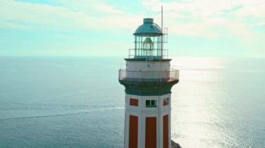 Sakin bir deniz feneri, gün batımının sıcacık parıltısında güneşlenerek denizin üzerinde nöbet tutar. Faro di Punta Carena, Capri, İtalya..