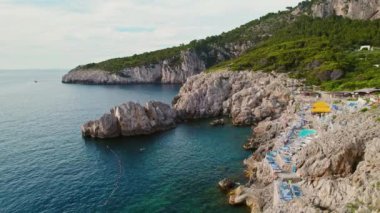 Turkuaz suları, uçurumları ve güneş banyosu yapan tenha bir sahil koy, havadan görülüyor. Lido del Faro Plajı Kulübü ve restoranı Capri, İtalya..