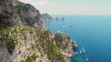 Bereketli yeşil kayalıklar kayıklarla benekli safir bir denize dalar. Yüksek uçurumları olan deniz burnu Faraglioni. Capri Adası, İtalya..