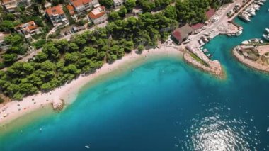 Turkuaz deniz suları olan bir sahil manzarası. Çam ağaçlarının yemyeşil yapraklarıyla sarılmış ve boş teknelerle benekli kıyı şeridi. Yaz Hırvatistan..