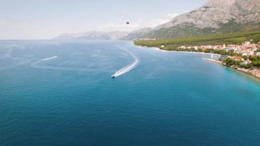 Açık mavi deniz manzaralı sürat tekneleri su yüzeyinde beyaz izler yaratıyor. Hırvatistan 'ın sakin Makarska kıyı kasabasında paraşütle atlama macerası görüldü. Yaz tatilleri..
