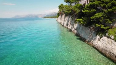 Gök mavisi denizi gören kayalık kayalıklara gür çamlar taç takar. Derin maviden açık sığlıklara su geçişi..