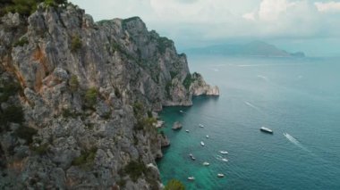 Capri kıyılarında kayalıklar ve sakin deniz sularında tekneler. Yaz günü İtalyan Adası 'nın engebeli kıyıları. Doğa manzarasının havadan görünüşü..