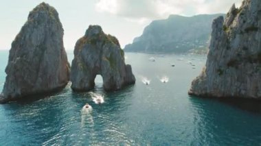 Yükselen deniz yığınları Faraglioni doğal bir geçit görevi görerek, her boyuttaki teknelerin taşıdığı canlı su yolunu çerçeveliyor. İtalya, Capri 'deki Akdeniz manzarasının huzur mavisi...