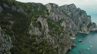Capri 'nin yamaçları deniz sularına ve demirli yatlara bakıyor. Doğal kemer oluşumları ve engebeli kıyı şeridi, aşağıdaki sakin körfezde deniz gemileri var...