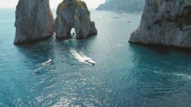 Capri Adası 'nda, Faraglioni kayalıkları ile hareketli bir denizin arka planına karşı. Sürat tekneleri suyu keserek arkalarında beyaz köpük izleri bırakırlar...