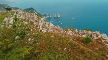Yazlık Elbiseli Kadın Sahil Vista 'nın tadını çıkarıyor. Turistler deniz manzarasına, Faraglioni kayalıklarına ve yüksek görüş açısına sahip teknelere hayran. Capri Adası, İtalya..