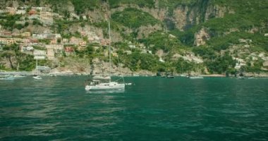 Positano 'nun çarpıcı arka planıyla çevrili bir yelkenli yat Amalfi kıyısı boyunca ilerliyor. Gemi, İtalya güneşinin altında Tyrhenian Denizi 'nde süzülüyor...