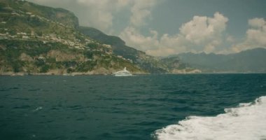 Positano köyü yakınlarındaki görkemli kıyı manzarası. Akdeniz mavisi deniz suları ve arka planda lüks yatları olan kayalıklar...