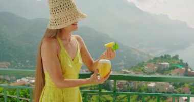 Yazlık elbiseli ve hasır şapkalı bir kadın limon dilimini ısırıyor. Üstünde krem şanti olan şerbeti tutan kız...