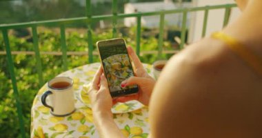 Amalfi terasında akıllı telefon kullanarak limon ve çay fotografı çeken eller. İtalyan güneşinin altında neşeli bir kahvaltı atmosferi..