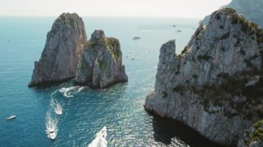 Tekneler ve yatlar Capri 'de Faraglioni' deki yüksek istiflerin yakınındaki sularda yol alırlar. Deniz manzarası hareketlilikle doludur, yüzeyi gemilerin kalıntıları tarafından oyulmuştur...
