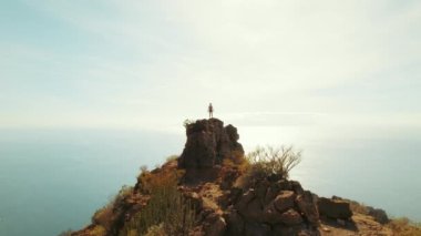 Kadın Tenerife 'de kayalık bir tepenin üzerinde duruyor, aşağıdaki engin okyanusa bakıyor. Los Gigantes kayalıklarının sakin güzelliği açık bir günde..