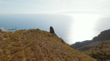 Kayalık bir arazide, açık bir kaya oluşumu, güneş ışığı ve çorak deniz üzerinde. Engebeli manzara, doğal kuraklığın altını çiziyor...