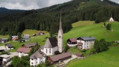 Yeşil bir vadiye kurulmuş bir köyün havadan görünüşü, yüksek kulesi ve orman tepeleriyle çevrili seçkin bir kilisenin görüntüsü...