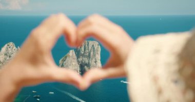 İtalya 'ya yaz gezisi sırasında Faraglioni kayalıklarını ve Capri Adası denizini çerçeveleyen ellerle yapılmış bir kalp şekli...