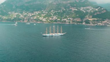 Arka planda teraslı tepeler ve Amalfi Sahili yakınlarında birden fazla direği olan büyük bir yelkenli gemi...