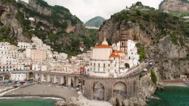Önde gelen kilisesi Santa Maria Maddalena ve arka planda engebeli uçurumları olan binaları olan Atrani kasabası...