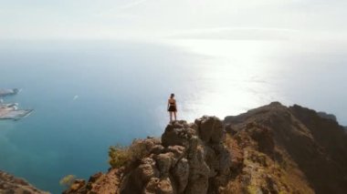 Tenerife 'de uçurumun kenarında duran kişi, ışıldayan denize bakıyor. Okyanus manzarası ve engebeli kıyı şeridi açılır..