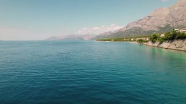 Camsı mavi deniz suyunda tek kişilik kürek. Kayalıklar ve evler, yaz günü açık bir gökyüzünün altında sakin sahili kaplar. Hırvatistan 'da tatiller..