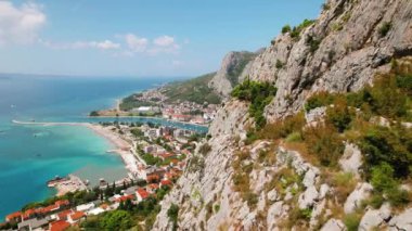 Omis kasabasının sahil şeridini tarıyor. Deniz ve kayaların arasına yerleşmiş, hareketli şehrin yukarısındaki dağlarda yürüyüş yapan kadın. Kırmızı çatılar ve deniz manzarası...