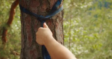 Bir kadının elini ağaca bağlarken, çam ormanında hamak kurarken..