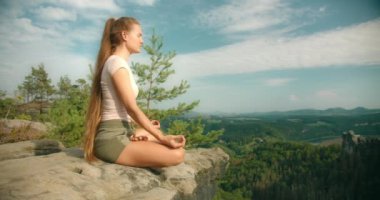 Uzun saçlı bir kadın, engin ormanlara ve uzak dağlara bakan bir kaya çıkıntısında lotus pozisyonunda meditasyon yapar...