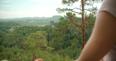 Bir kadın, Almanya 'nın Bastei bölgesindeki geniş ormanlık vadiyi ve uzak dağları alarak yüksek bir kaya çıkıntısı üzerinde meditasyon yapıyor..