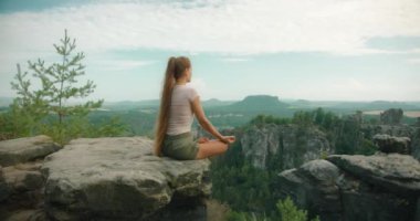 Uzun saçlı bir kadın kayalık bir çıkıntıda meditasyon yapıyor. Bastei kaya oluşumlarının ve etrafındaki ormanın geniş manzarasına bakıyor...