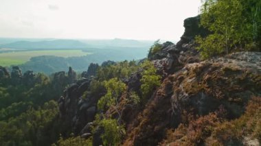 Yürüyüşçüler kayalık kayalıkları keşfederek kayalık tepeleri ve yumuşak güneş ışığıyla yıkanan çentikli kaya oluşumlarını inceliyor. Elbe Kum Taşı Dağlarında Schrammsteine..