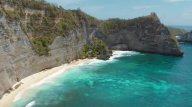 Yüksek kayalıkların altında tenha bir sahil. Parlak güneşli bir günde turkuaz dalgalar beyaz kuma çarpıyor...
