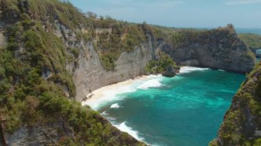 Dik uçurumları ve turkuaz suları olan gizli sahil koyunda, engebeli kaya oluşumlarıyla çerçevelenmiş, Elmas Sahili, Nusa Penida..