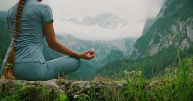 Kadın, sakin bir göl ve arkada sis kaplı dağlarla bir kayanın üzerinde meditasyon yapıyor..