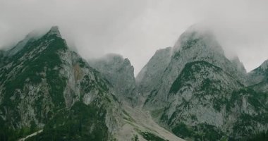 Dik yamaçları ve yemyeşil yeşillikleri olan bulutlu bir dağ silsilesi..