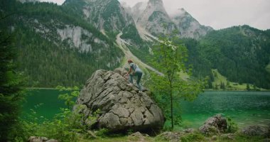 Yeşil ormanları ve dik dağları olan manzaralı dağlık bir gölün yanındaki kayaya tırmanan bir kadın..