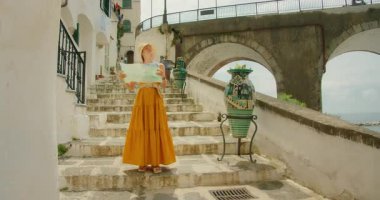 Sarı elbiseli kadın, Atrani İtalyan sahil kasabasında eski taş basamaklarda harita üzerinde çalışıyor..