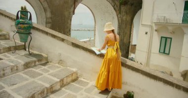 Sarı elbiseli kadın İtalya 'nın Atrani şehrinde deniz kenarında taş merdivenlerde harita okuyor..