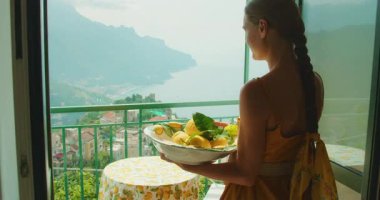 Yaz boyunca Amalfi sahilinde bir balkonda limon kasesi taşıyan bir kadın..