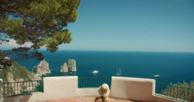 Kadın, güneşli bir yaz gününde Faraglioni kayalarının ve Capri Adası 'ndan gelen mavi denizin tadını çıkarıyor...