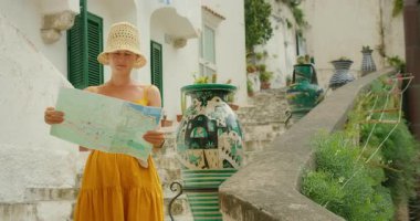 Turist, İtalya 'nın Amalfi kıyısındaki Atrani şehrinde yaz günü merdivenlerde duran vazonun yanında harita okuyor..