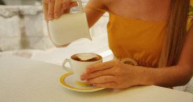 İtalyan şehrinde yaz günü kahve masasında kahveye süt döken bir kadın..