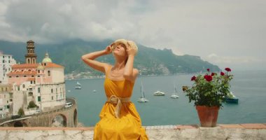 İtalya 'nın Atrani şehrinde deniz manzaralı terasta şapkasının altına bakan bir kadın..