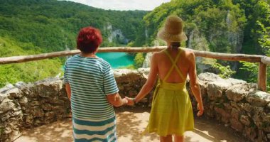 Bereketli kanyon ve mavi nehir manzaralı iki arkadaş arasında neşeli bir beşlik. Hırvatistan 'ın Plitvice Gölleri Ulusal Parkı' nda yürüyüş yapan kadınlar..