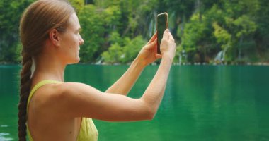 Hırvatistan 'daki Plitvice Lakes Ulusal Parkı' nda turkuaz göl ve şelalelerin fotoğraflarını çeken kadın.