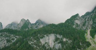 Bulutlu bir gökyüzünün altında yoğun ormanlarla çevrili keskin alp zirveleri macera hissi uyandırıyor..